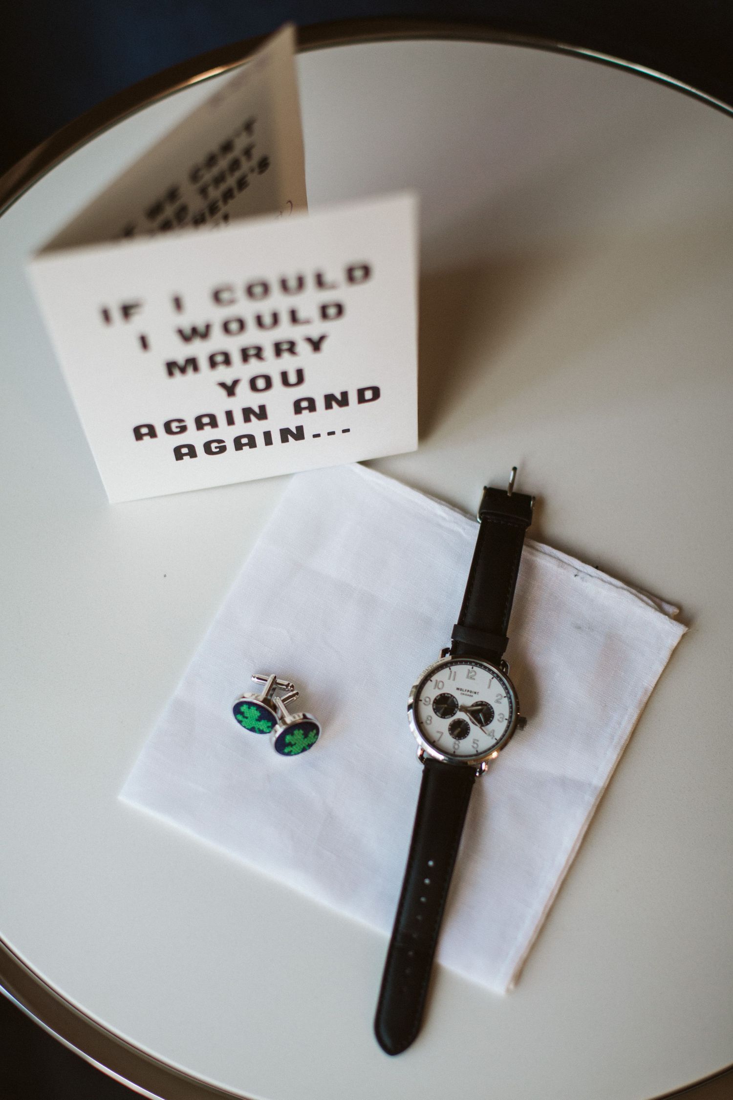 Wedding details including note cards, watch, and jewelry on white surface.