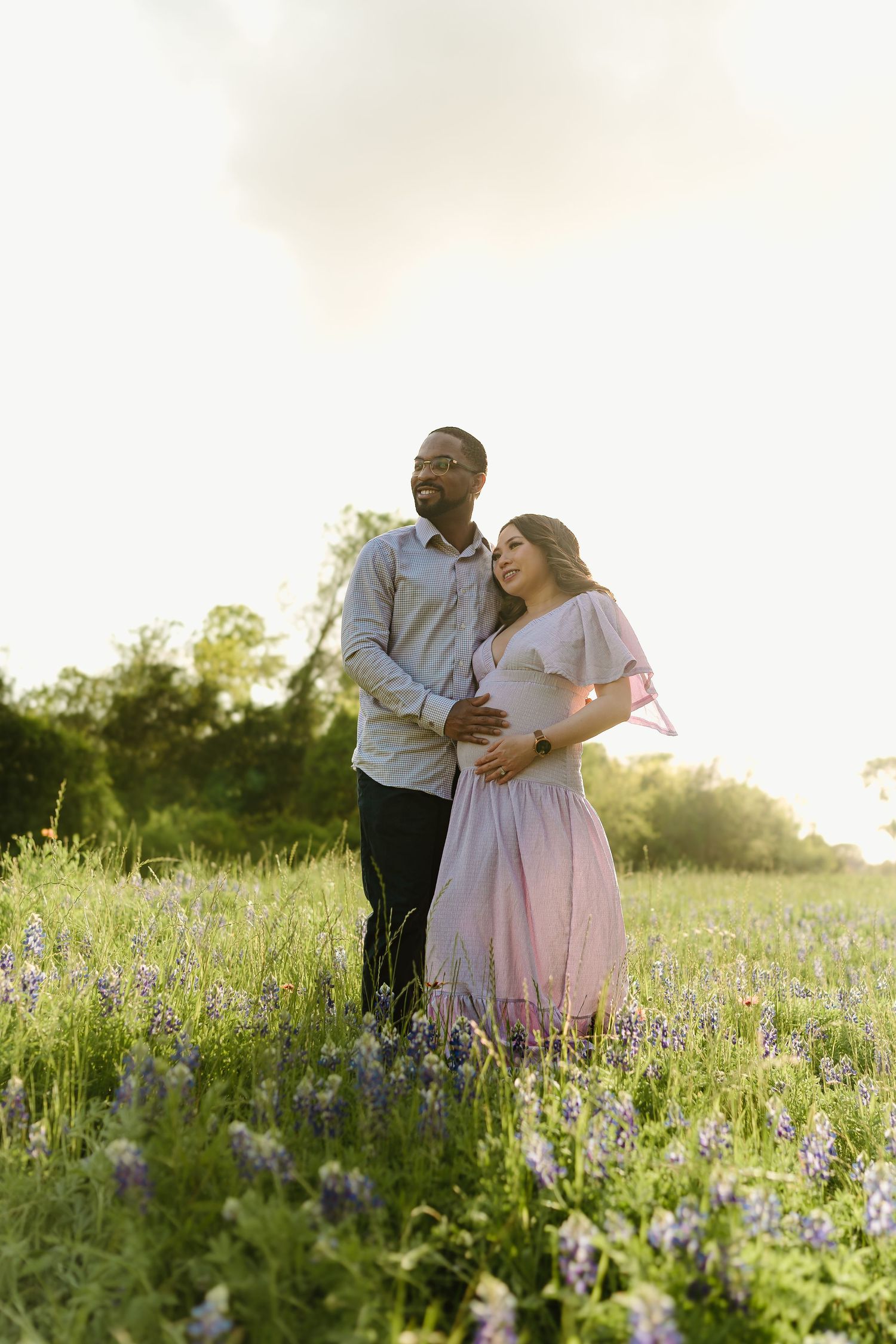 Couple embracing in a field of purple wildflowers during golden hour.