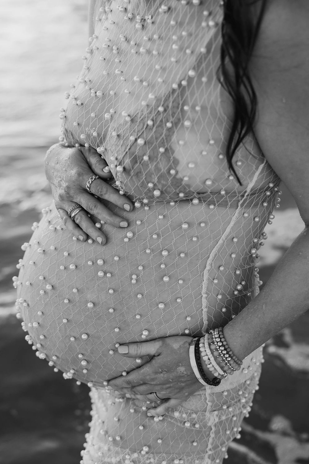 Artistic black and white maternity photo showing a close-up of a pregnant belly in a beaded sheer dress.