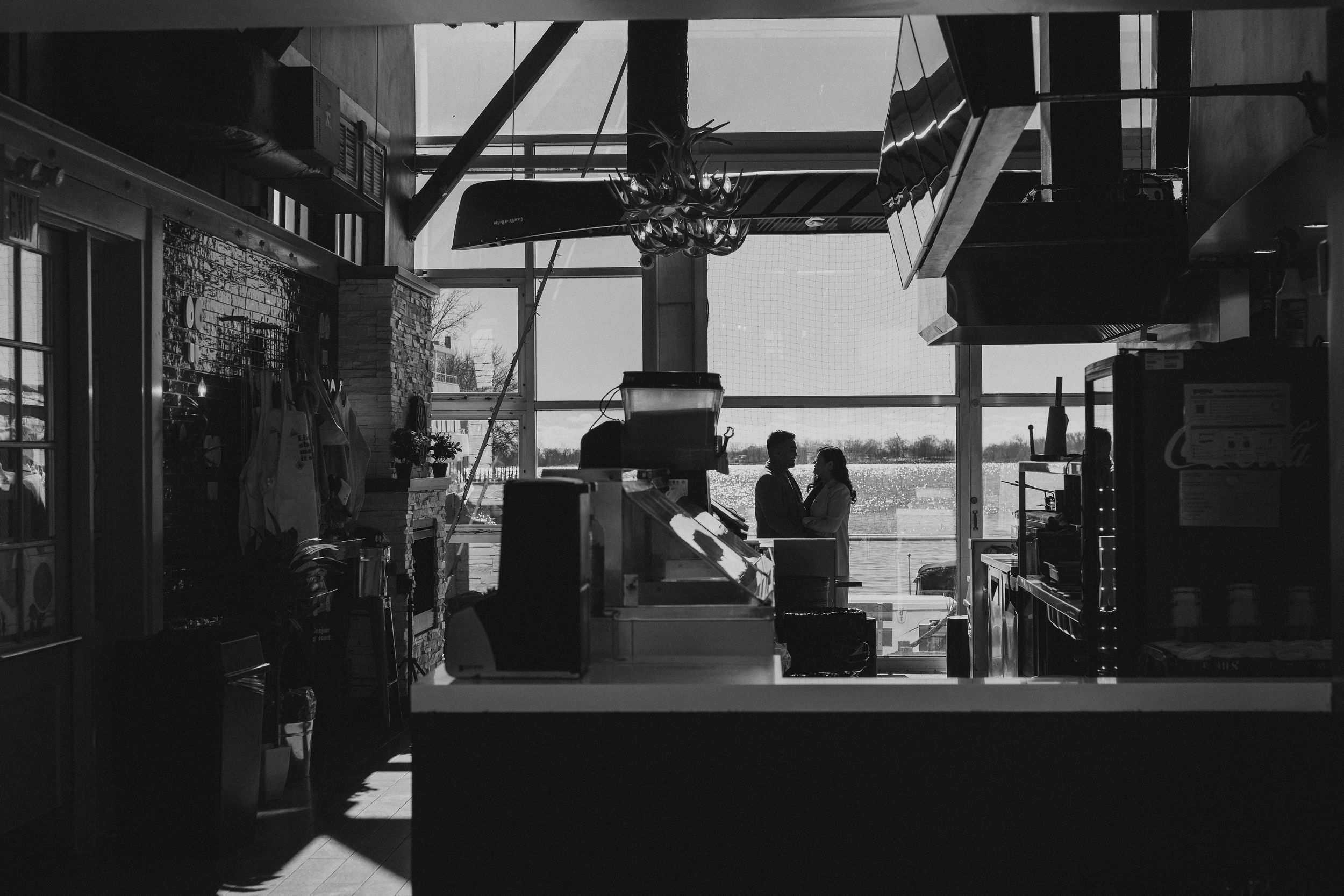 Silhouette of a kitchen or cafe interior with backlit windows and hanging fixtures creating a moody atmosphere.