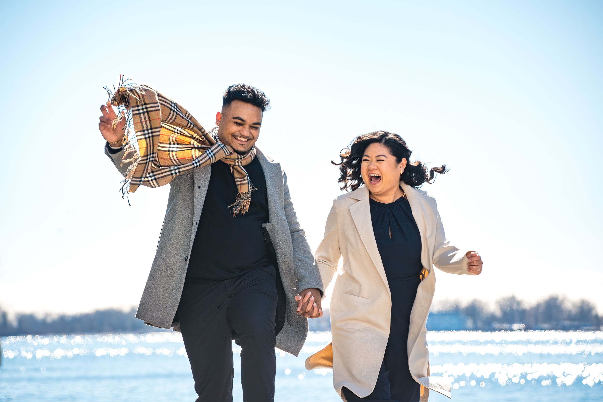 Happy couple enjoying a winter date by the water while holding a colorful blanket.