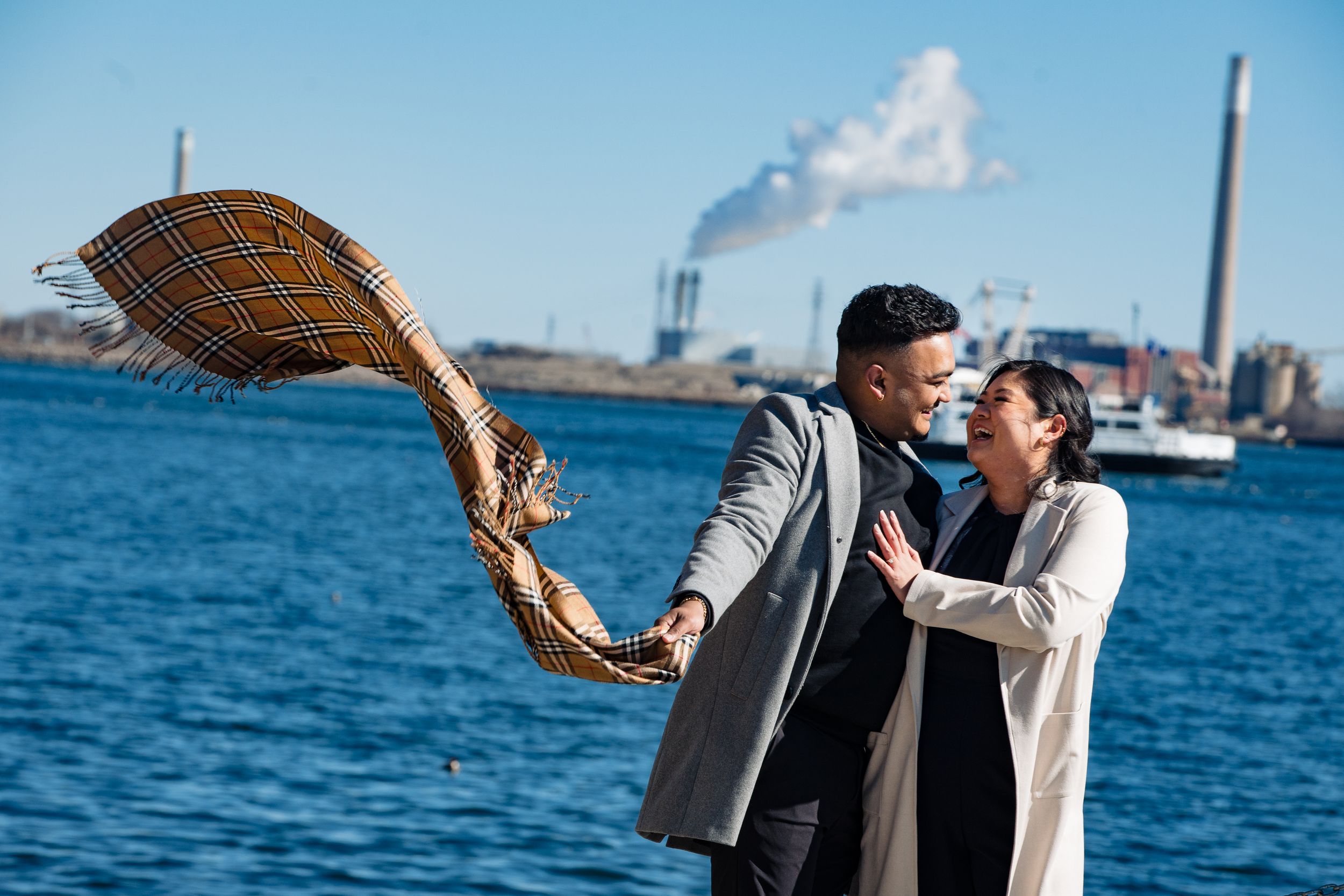 Joyful duo plays with a woven blanket against an industrial waterfront backdrop.