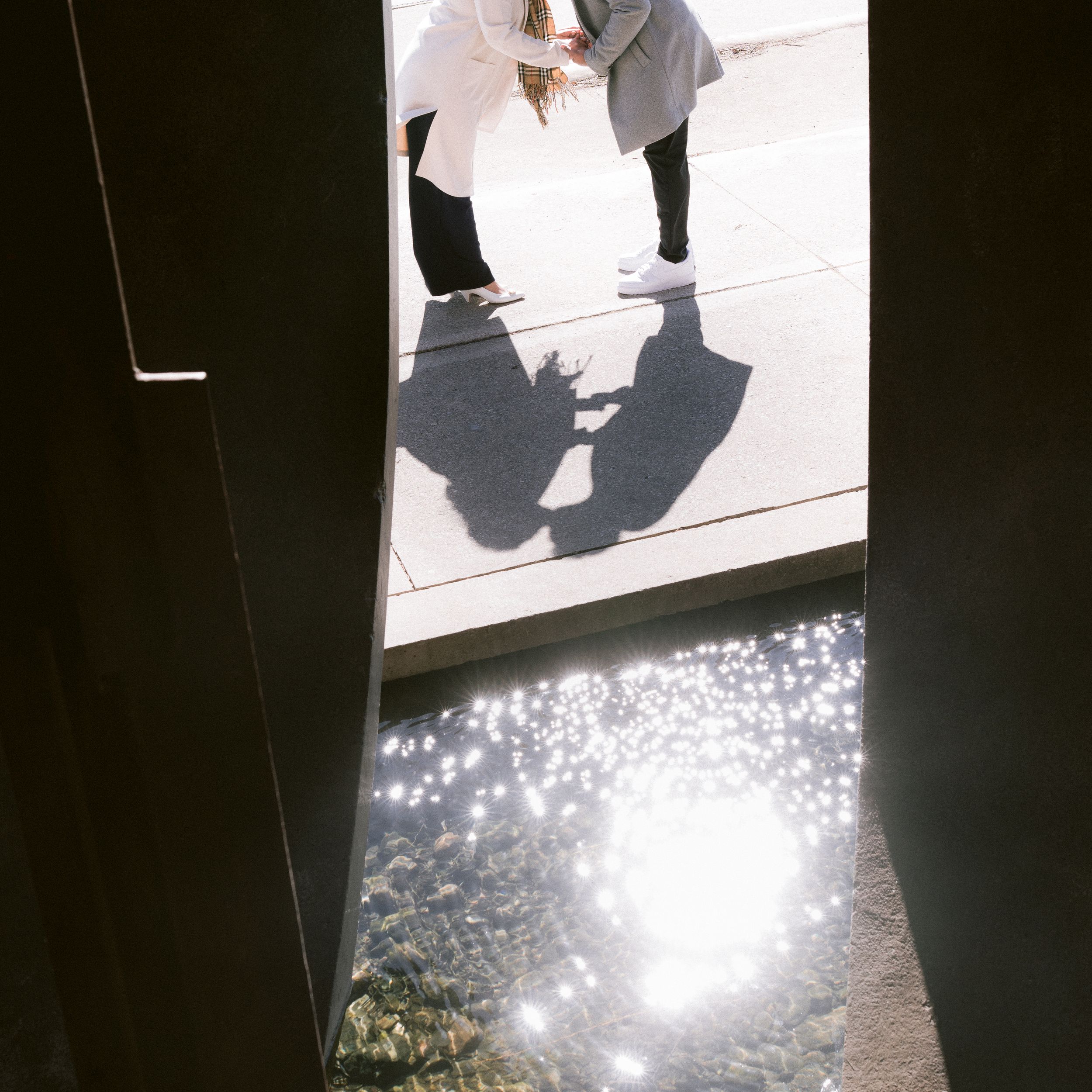 Shadows cast on concrete with glowing sunlit water reflection below casting sparkles and light.
