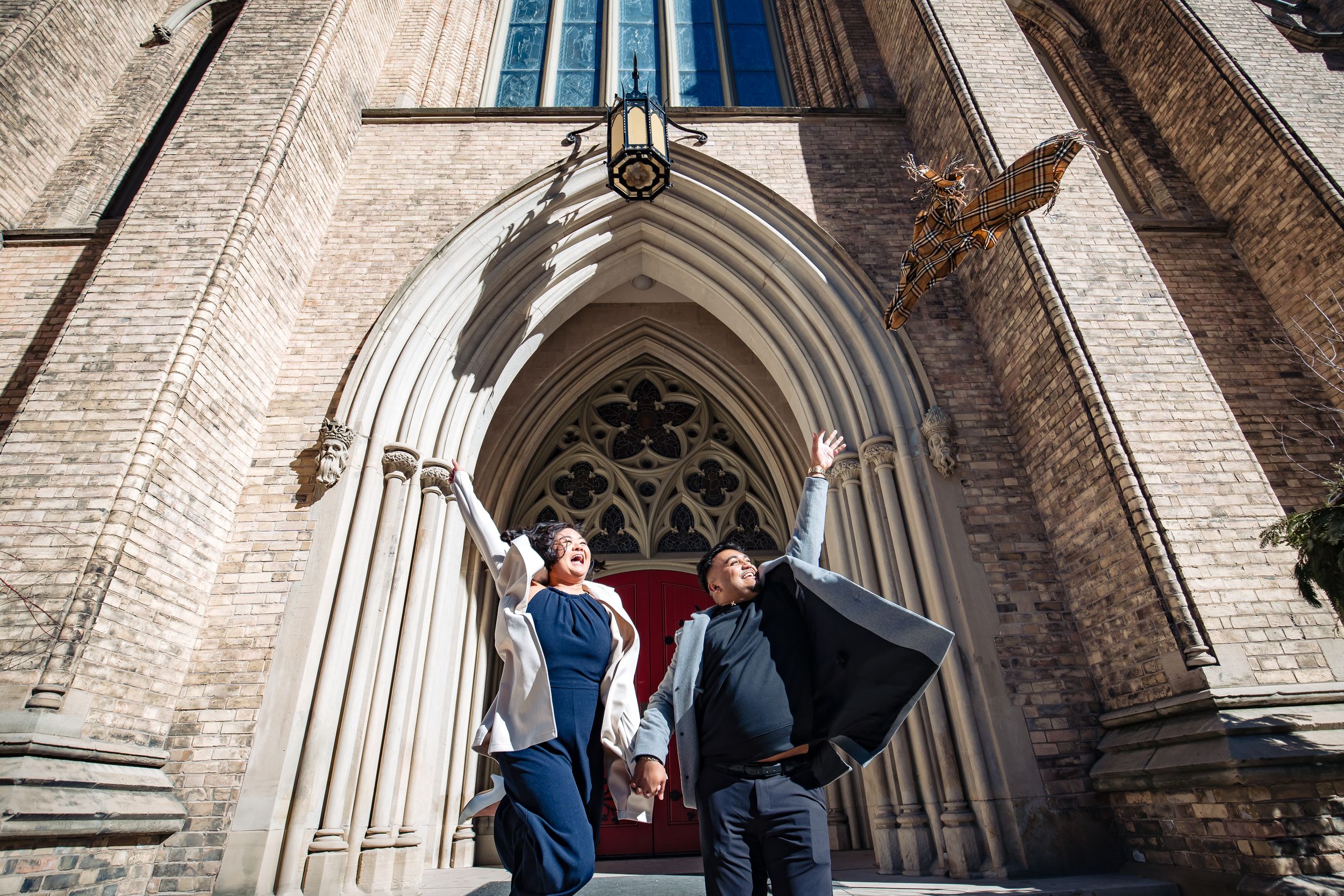 Three people pose in formal attire beneath a grand gothic church archway entrance.