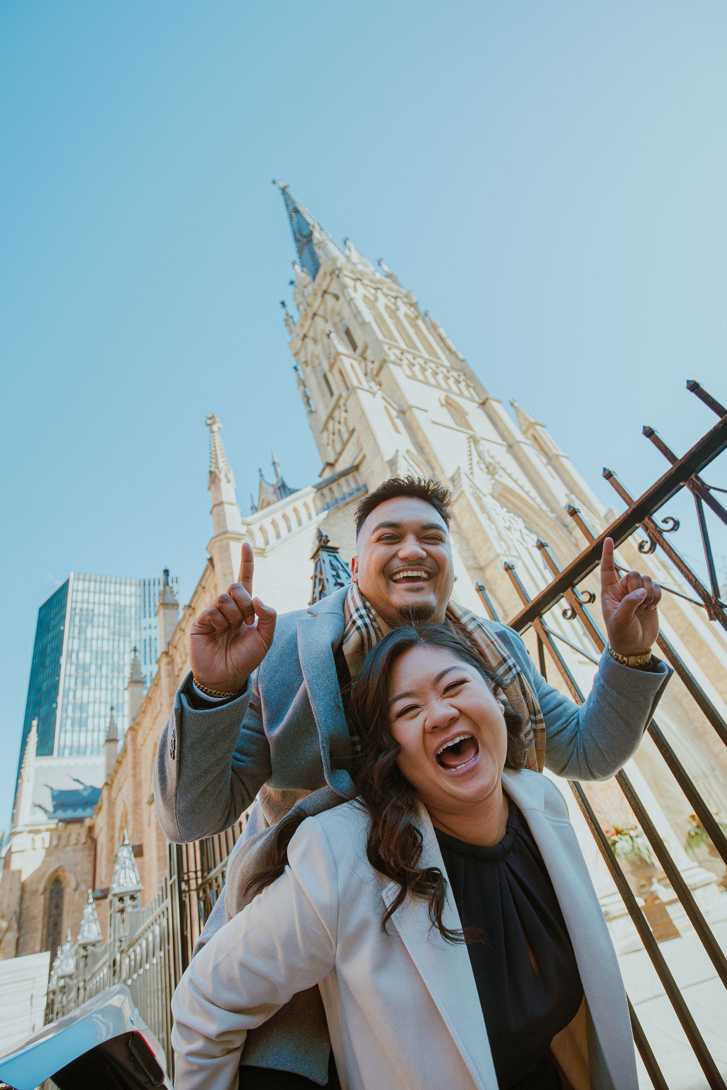 Two excited tourists pose in front of St. Patrick's Cathedral in New York City on a sunny day.