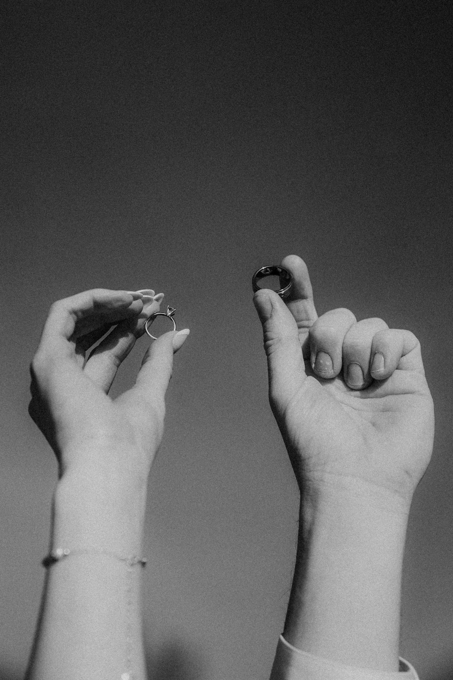 black and white image of bride and groom's hands holding up wedding rings