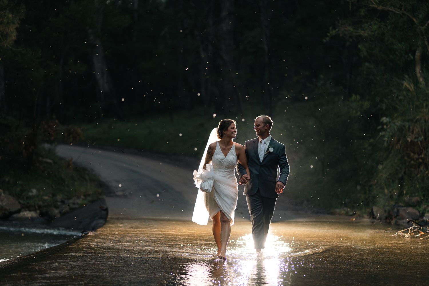 A bride and groom are walking through a shallow stream The bride is wearing a white dress and veil,and the groom is in a dark suit. Romantic