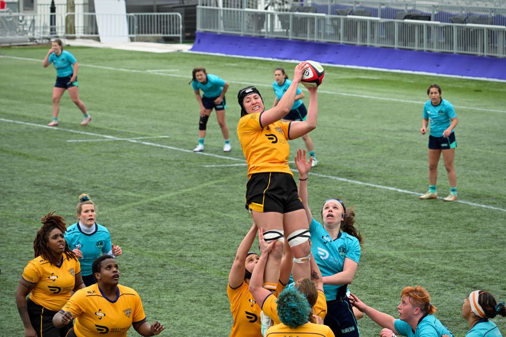 A Chicago Tempest athlete successfully catches a rugby ball thrown into play from the sidelines while New York Exiles players look on