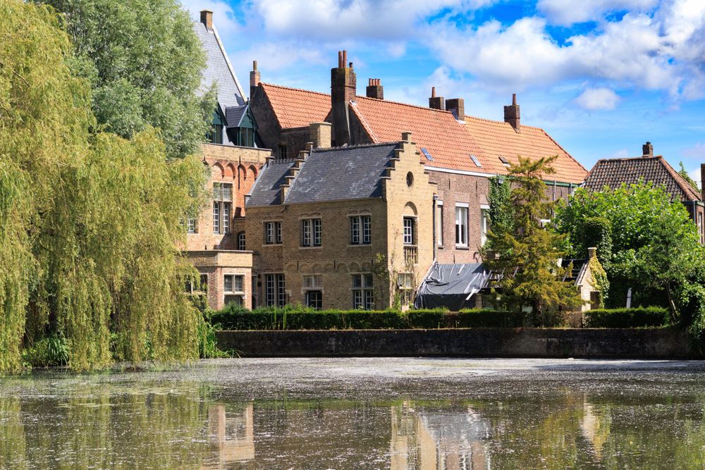 Traditional brick buildings with willow trees reflect in still waters of a medieval European canal.
