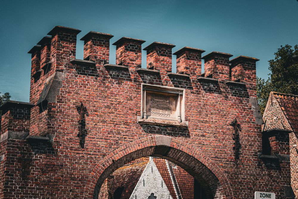 Medieval brick fortress wall with crenellations against deep blue sky in Bruges.