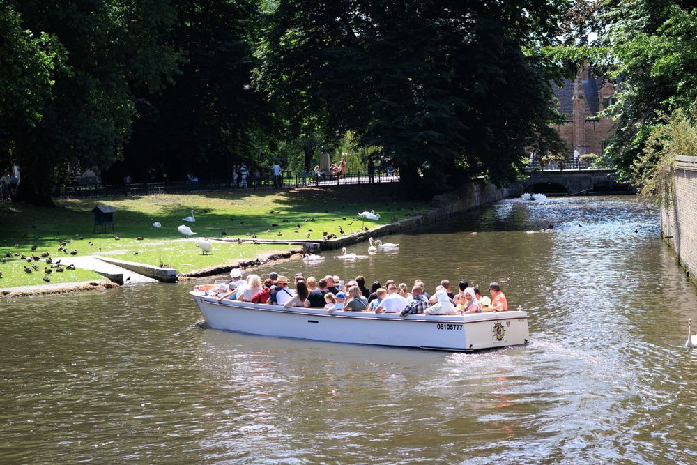 Tourist boats navigate through a scenic canal lined with trees and historic buildings.