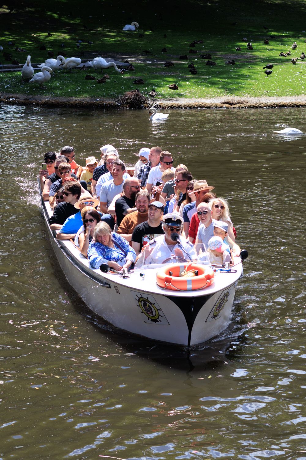 Tour boat filled with passengers cruises along a tranquil canal surrounded by greenery.