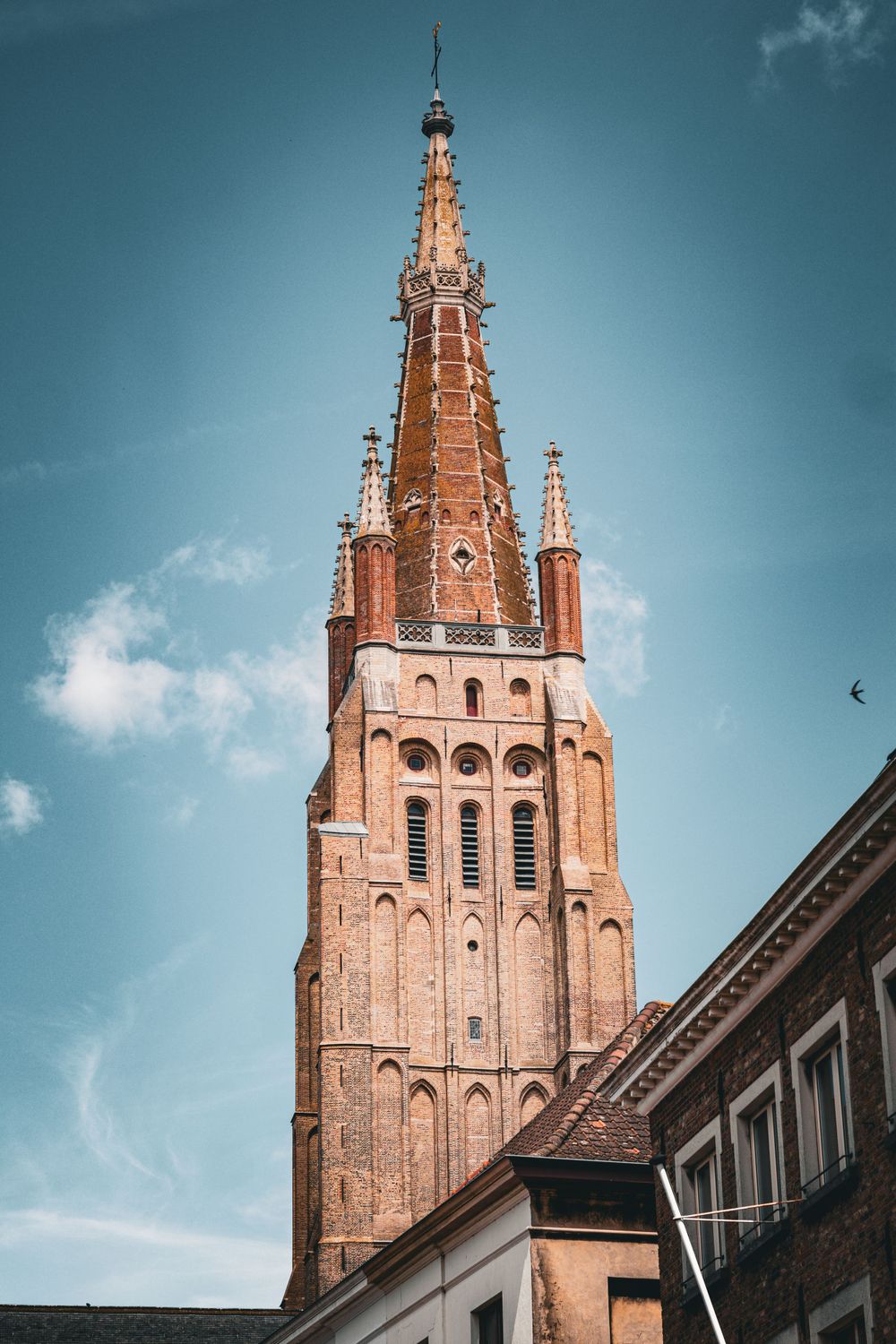 Ornate Gothic church spire rises against blue sky in Bruges city center.