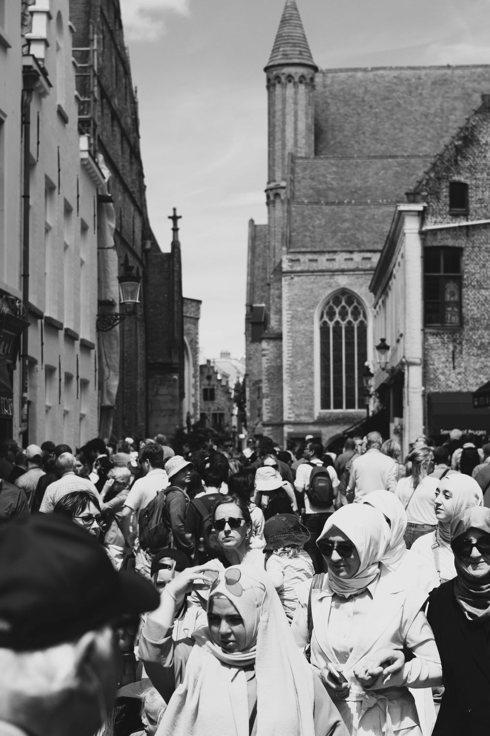 Black and white photo of crowds gathering near historic church buildings in Bruges.