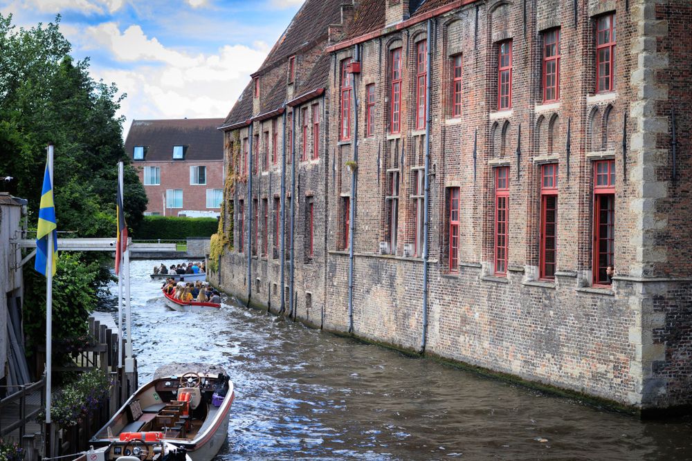 Historic brick buildings line a narrow canal waterway in medieval Bruges.