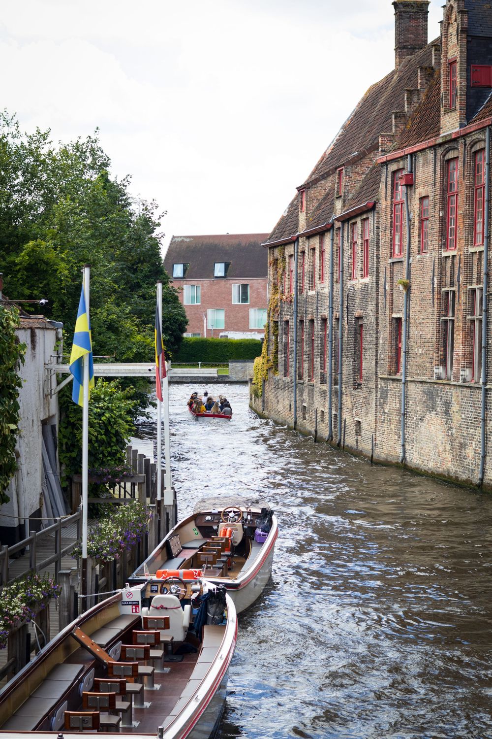 Tourist boats navigate through narrow canal between historic stone buildings in Bruges.