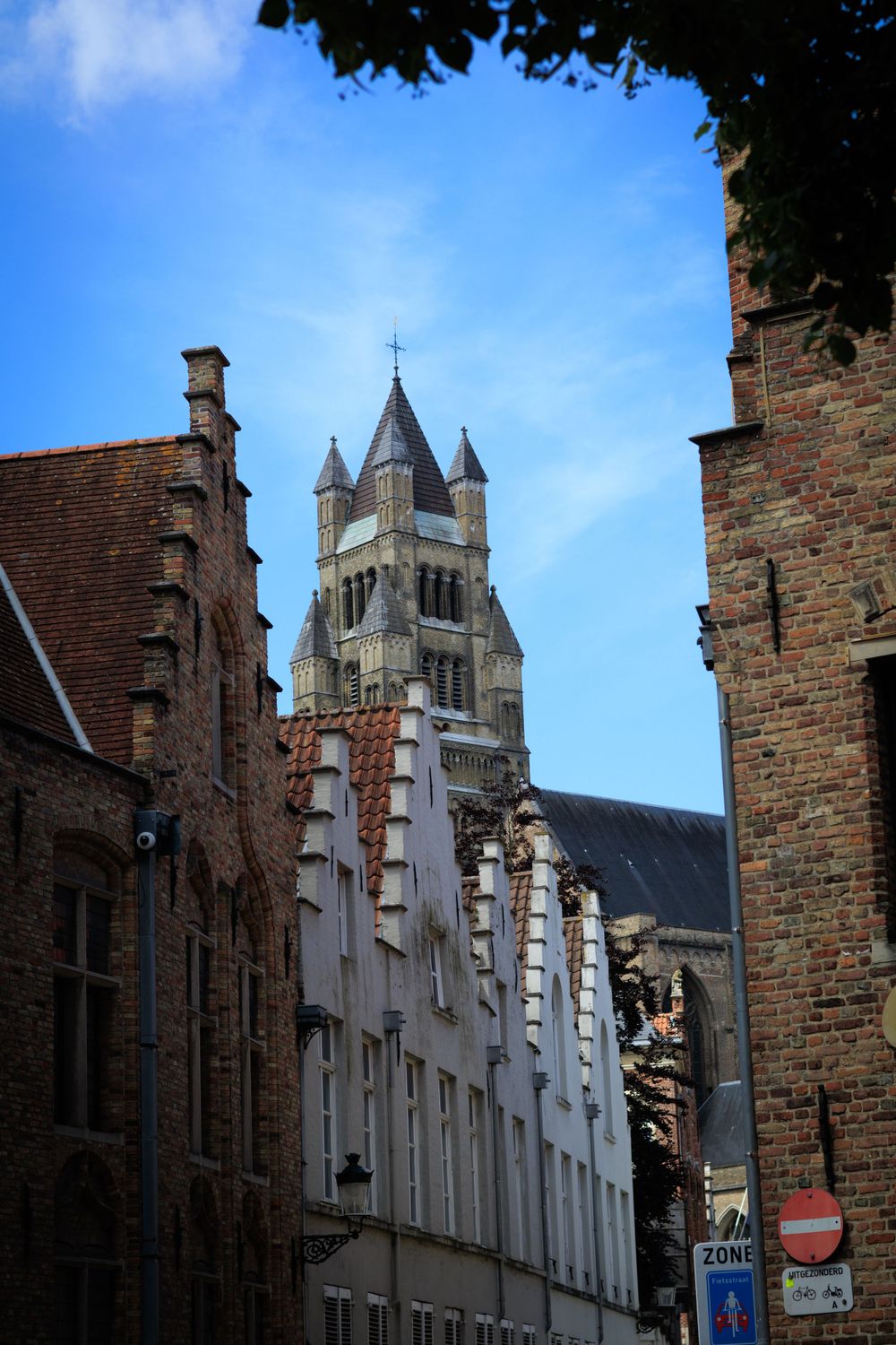 Medieval Gothic architecture with white stepped gables and towers rises against a blue sky in Bruges.