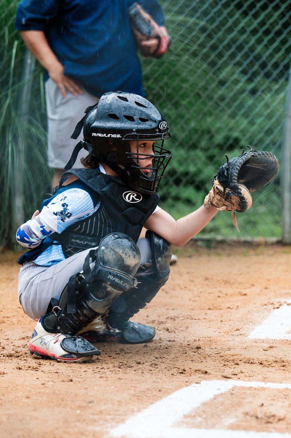 Youth baseball catcher in protective gear crouches behind home plate ready for the pitch.