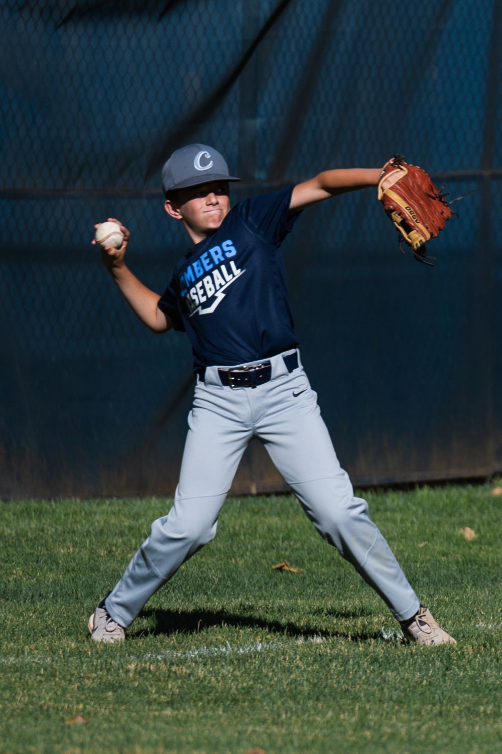 Baseball player in navy and gray uniform practices fielding positions on grass field.