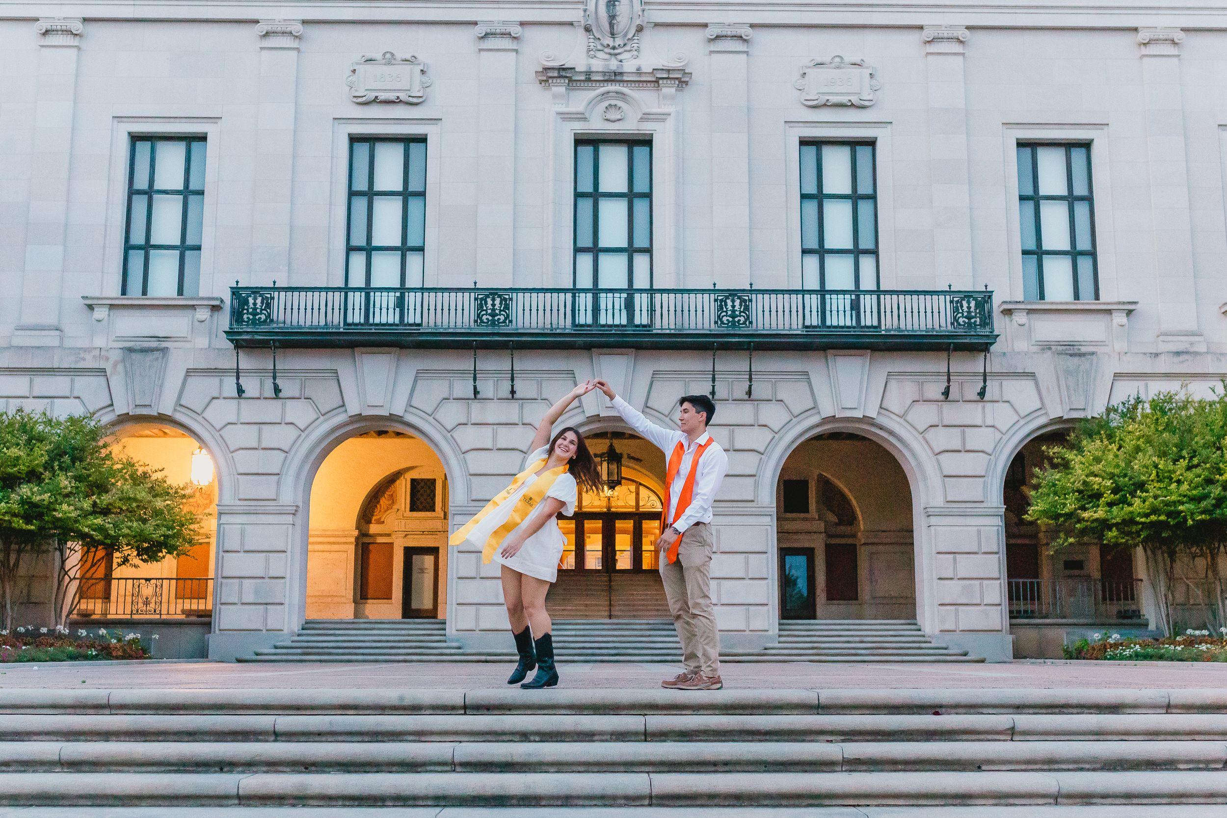 Graduate jumping for joy on stone steps of classical university building.