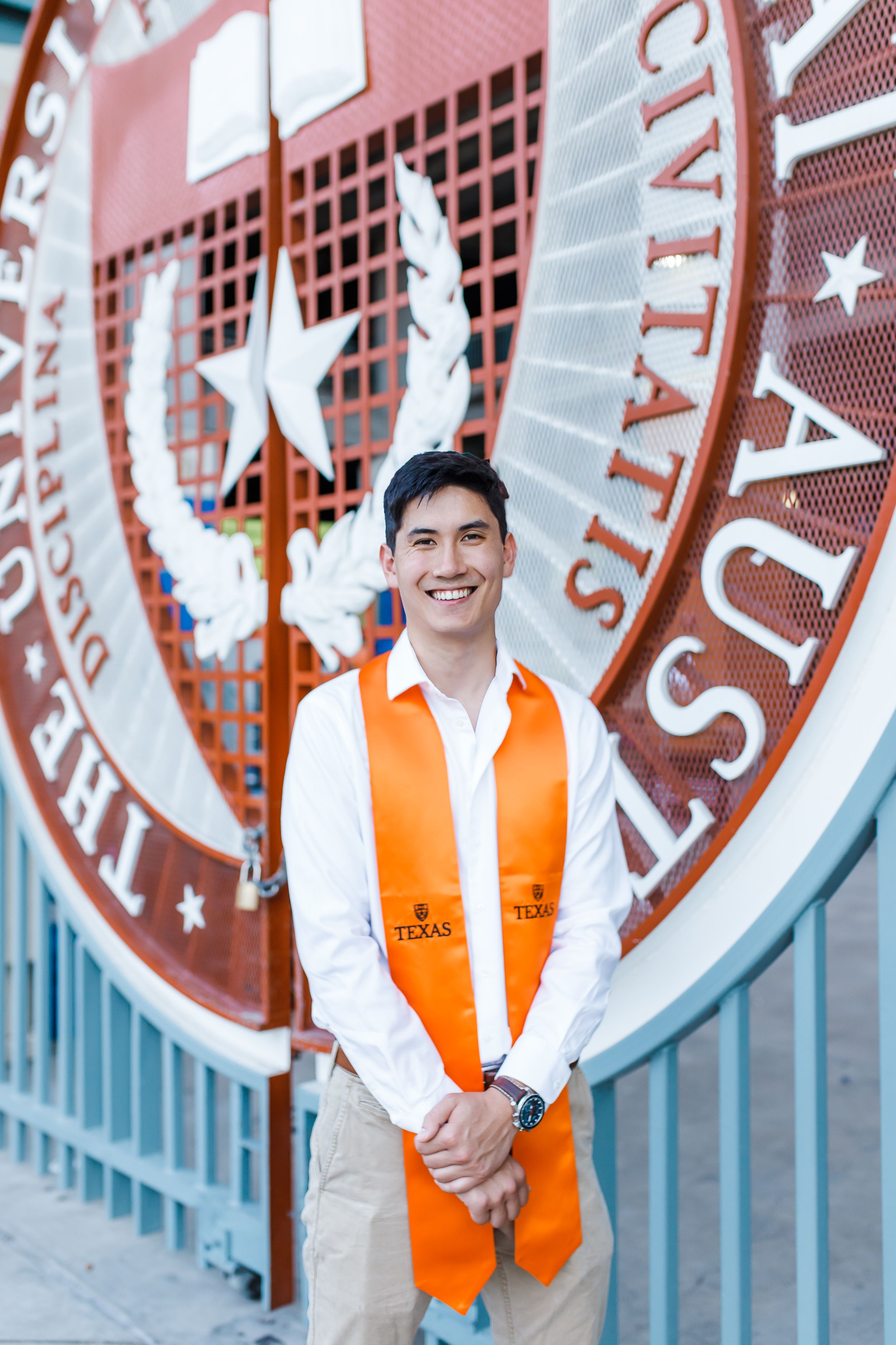 Graduate wearing orange stole standing in front of University of Texas seal.