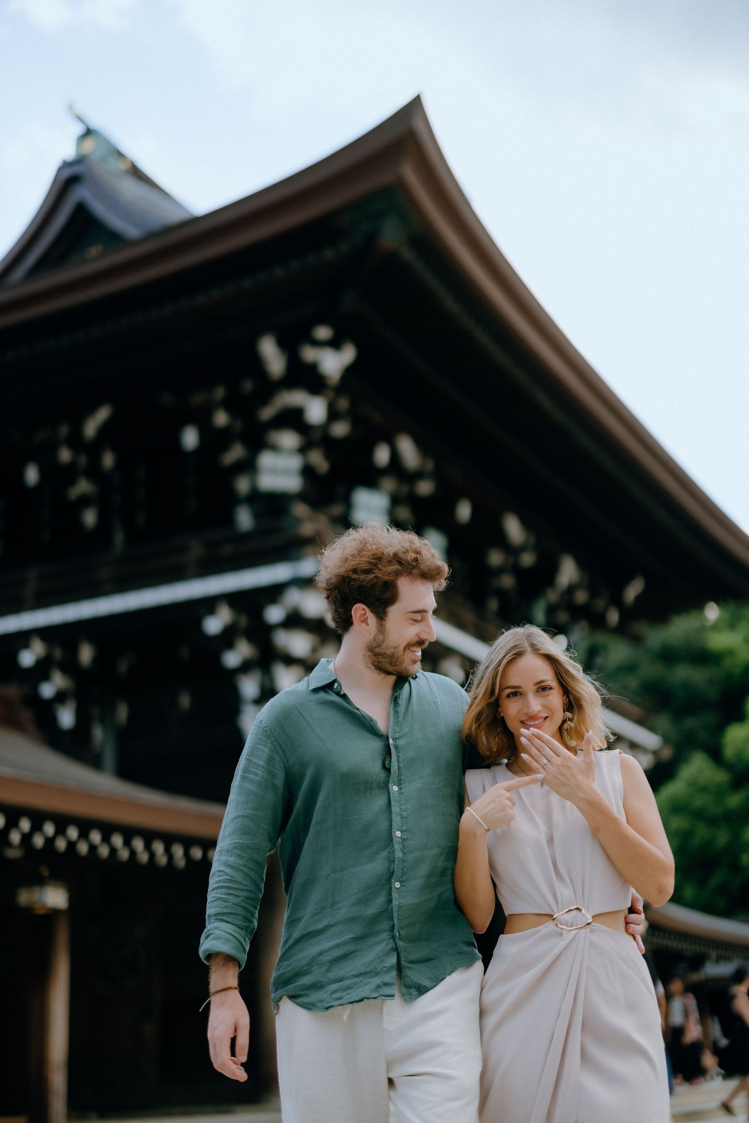 A couple explores the grounds of a traditional Japanese temple with ornate architectural details in the background.