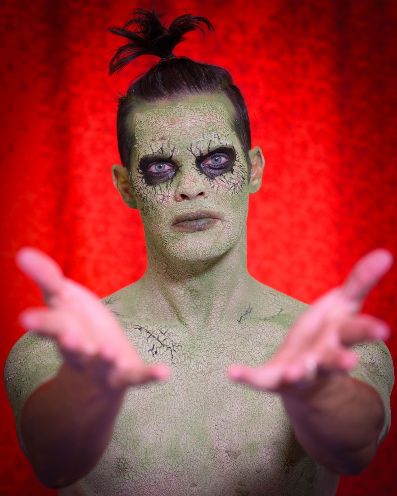 Dramatic red-lit portrait with theatrical makeup and outstretched hands.