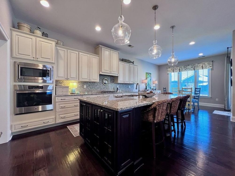Elegant modern kitchen with cream cabinets, dark wood floors, large black island and glass pendant lighting.