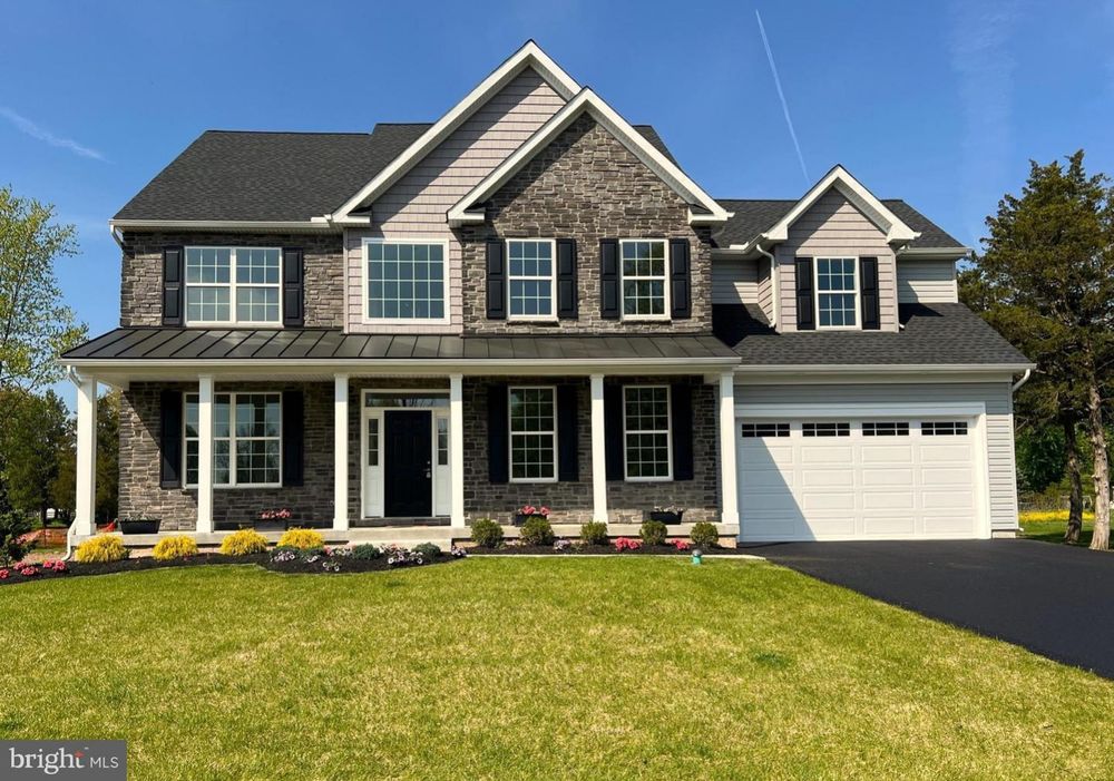 A large two-story suburban house with gray siding, white trim, dark shutters, and an attached garage set on a green lawn.