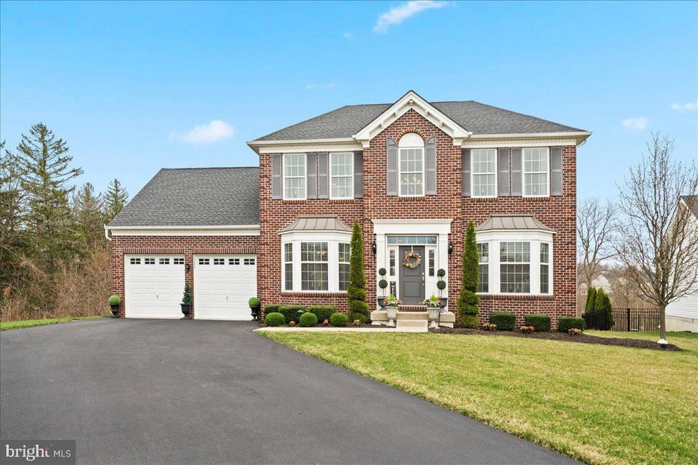 Large brick two-story colonial style home with white trim, arched windows, and attached two-car garage on landscaped lot.