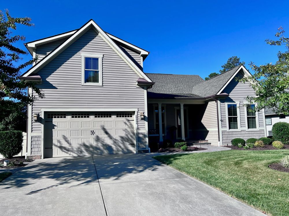Modern gray two-story home with attached garage, bay windows, and pristine landscaping on a sunny day.