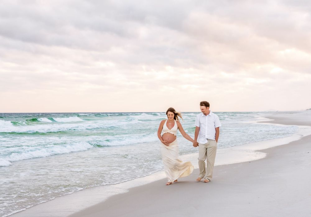 A couple walks hand in hand along a pristine white sand beach at sunset with turquoise waves rolling in.