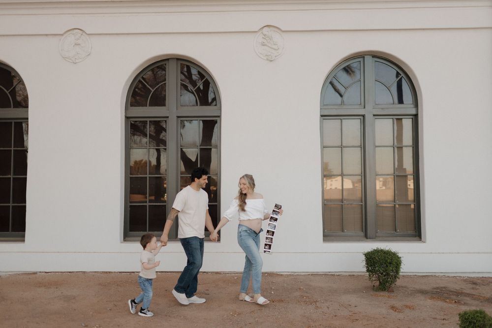 People walking along a white building exterior with arched windows.