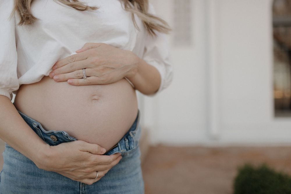 Close-up shot of hands embracing a pregnant belly in casual attire.