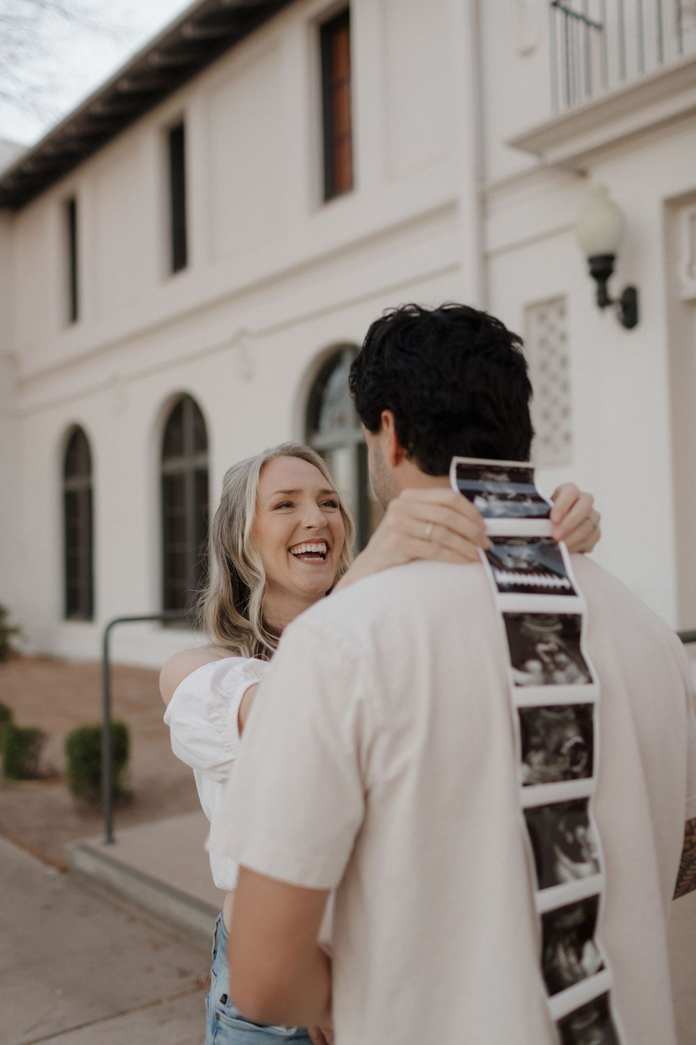 Happy couple sharing excitement while looking at ultrasound photos outside colonial building.
