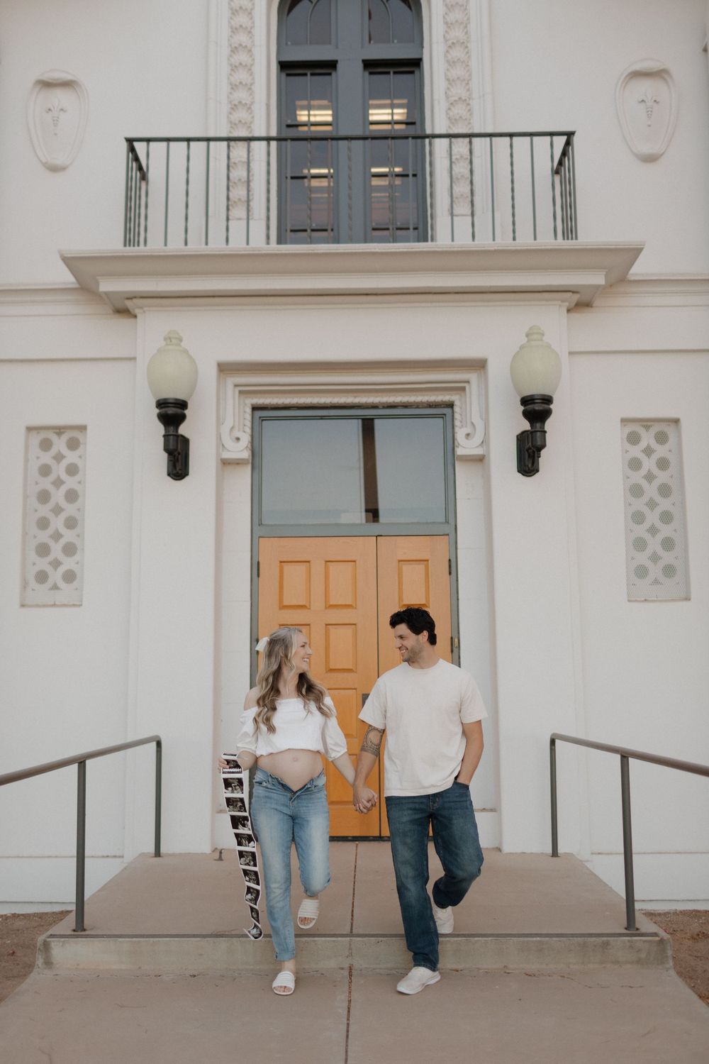 Couple posing at entrance of white Spanish colonial building with ornate balcony.