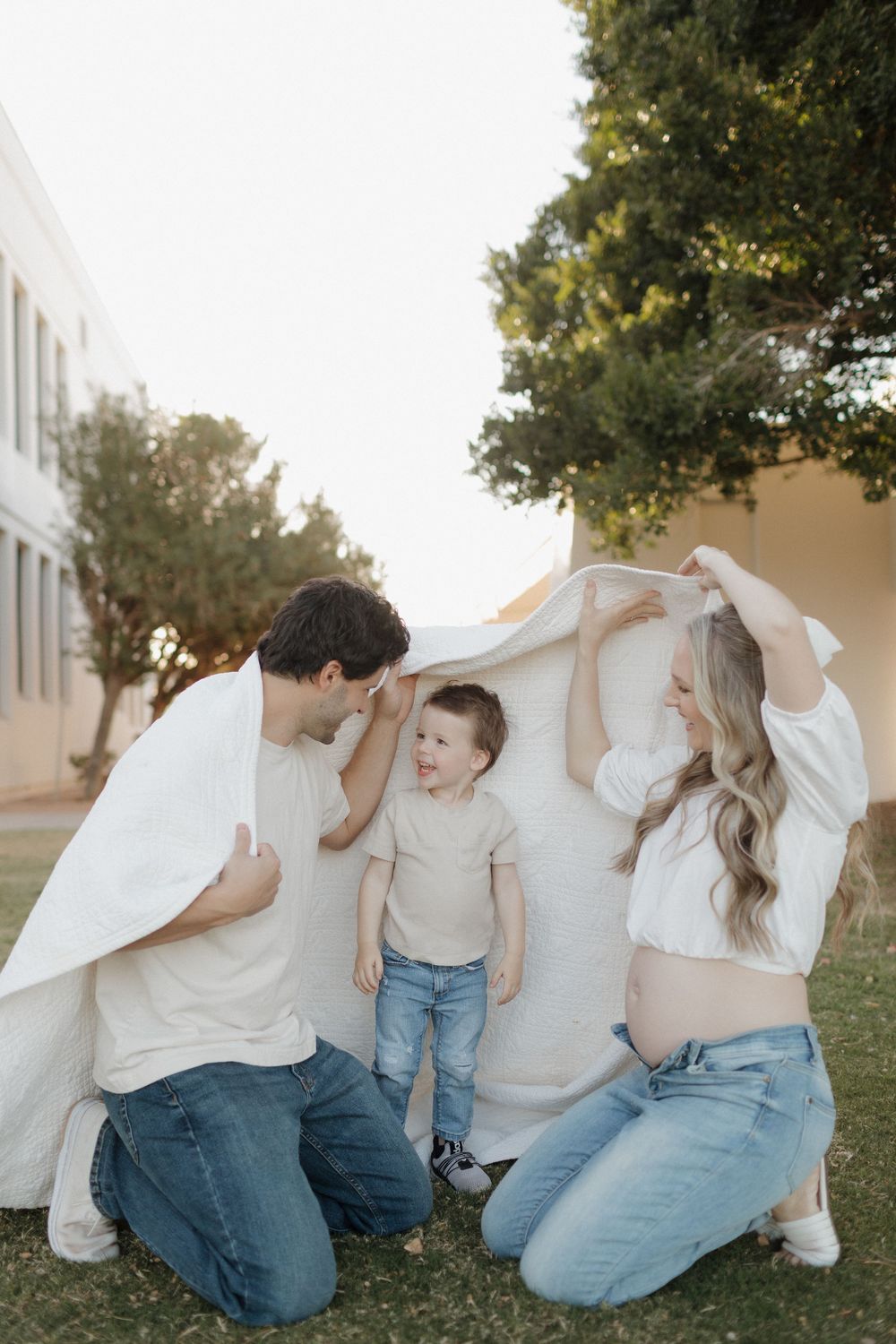 Family creates a cozy fort with white fabric while playing on grass.