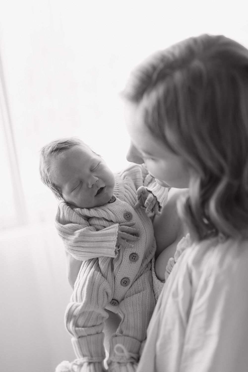 Black and white image of smiling baby in knit outfit being held.