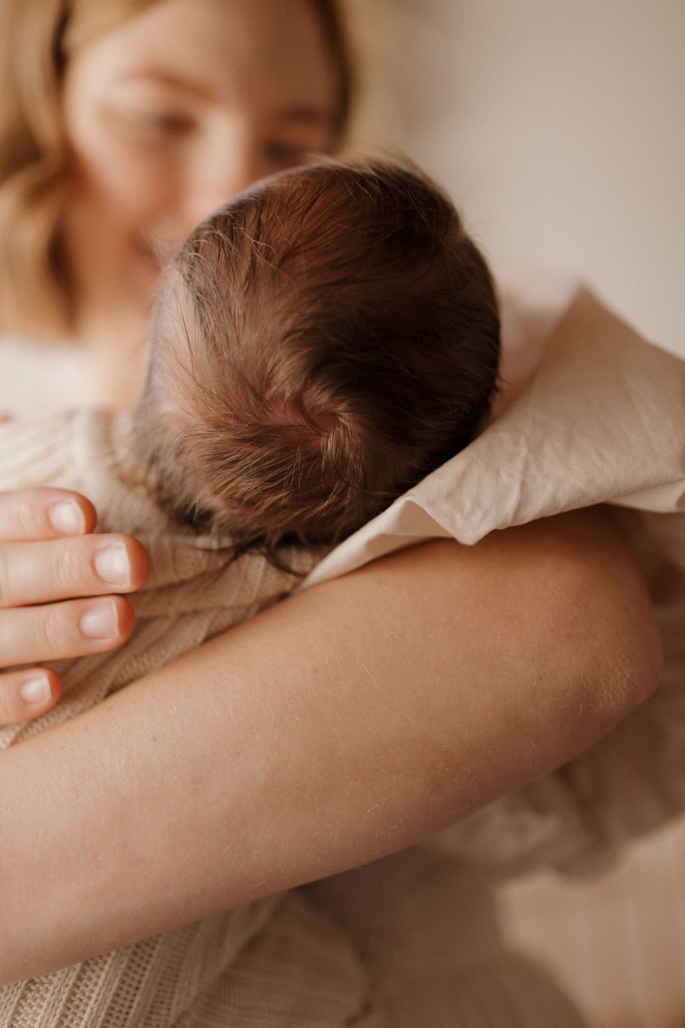Close-up view of infant with dark hair being cradled in soft natural lighting.