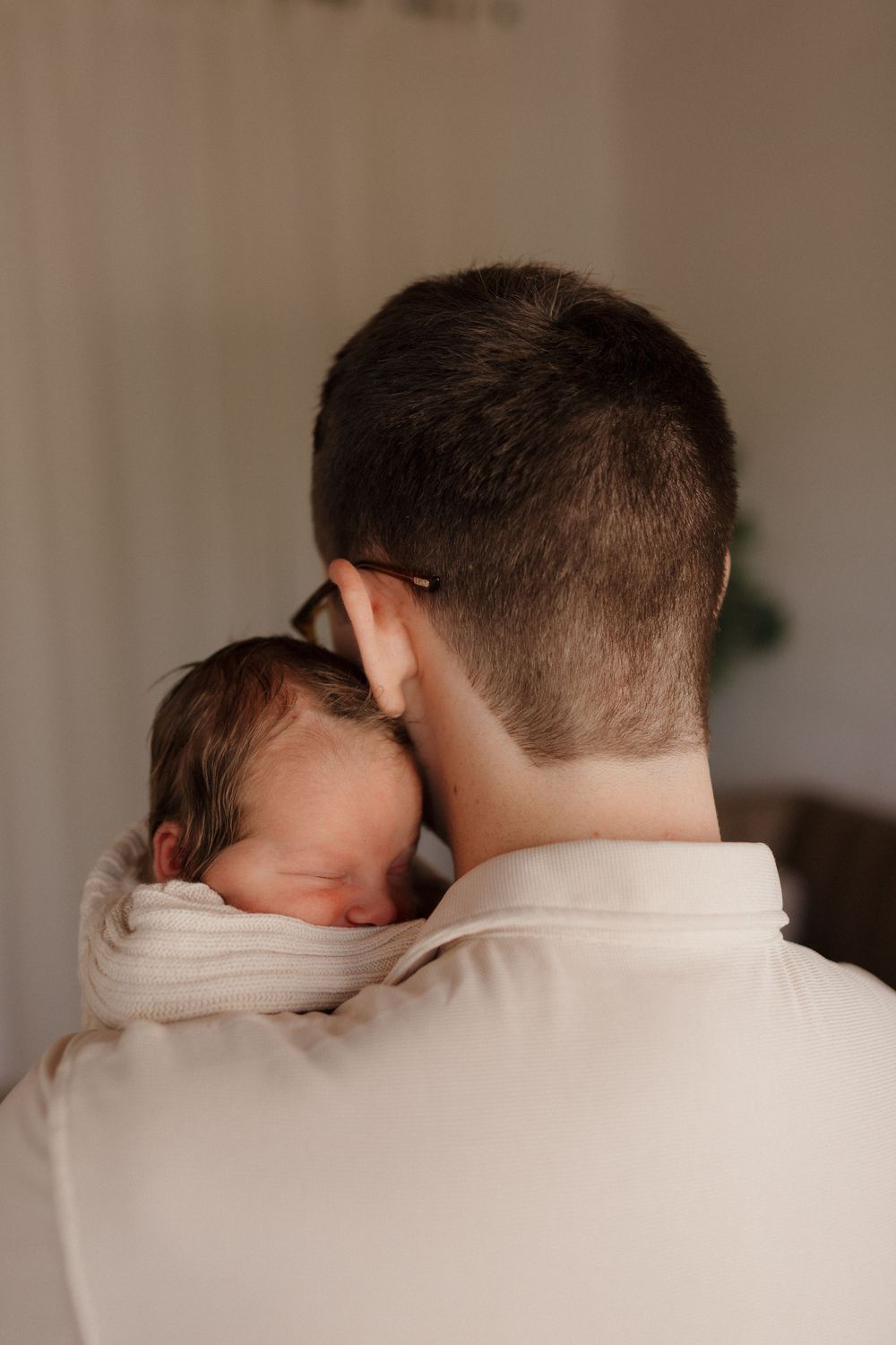 Over-shoulder view of sleeping newborn resting on adult's shoulder.