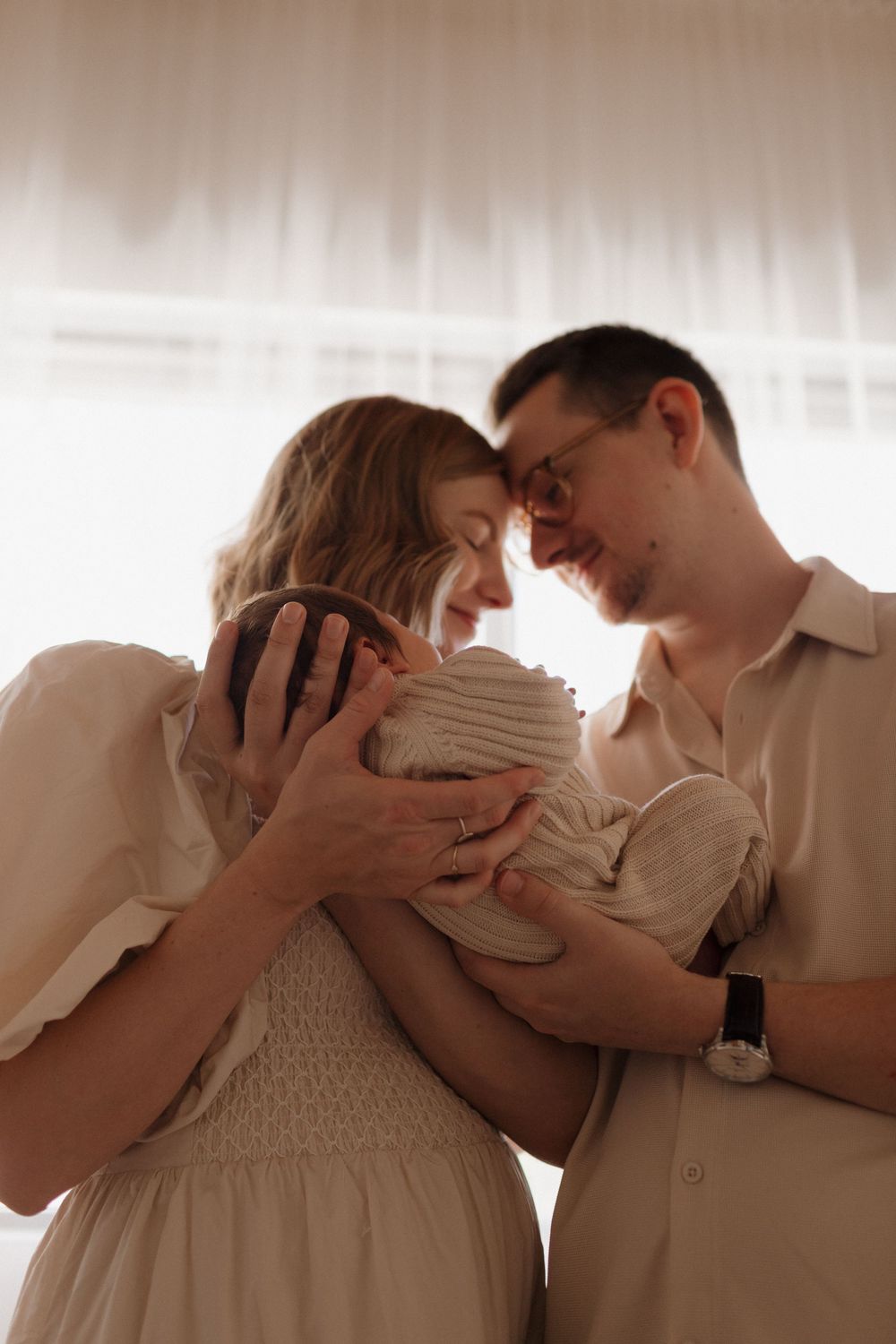A tender intimate moment between new parents holding a newborn baby in a softly lit room.