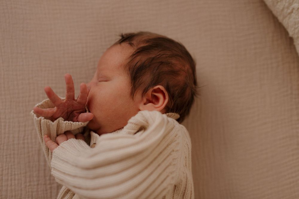 Sleeping newborn stretching arms in cream-colored ribbed sweater.