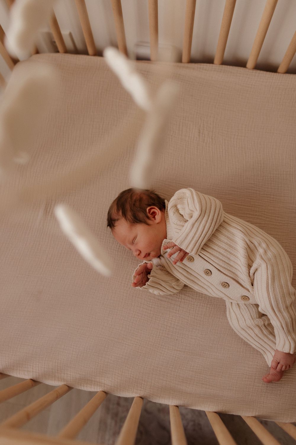 Overhead view of peaceful sleeping newborn in striped knitwear on cream bedding.