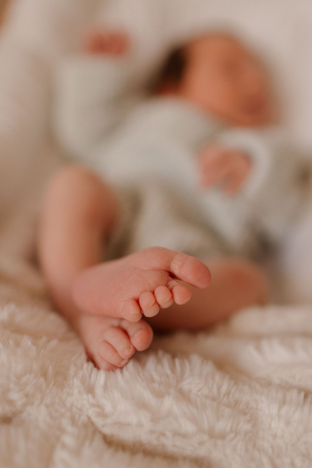 Close-up of tiny newborn feet resting on soft white textured fabric.