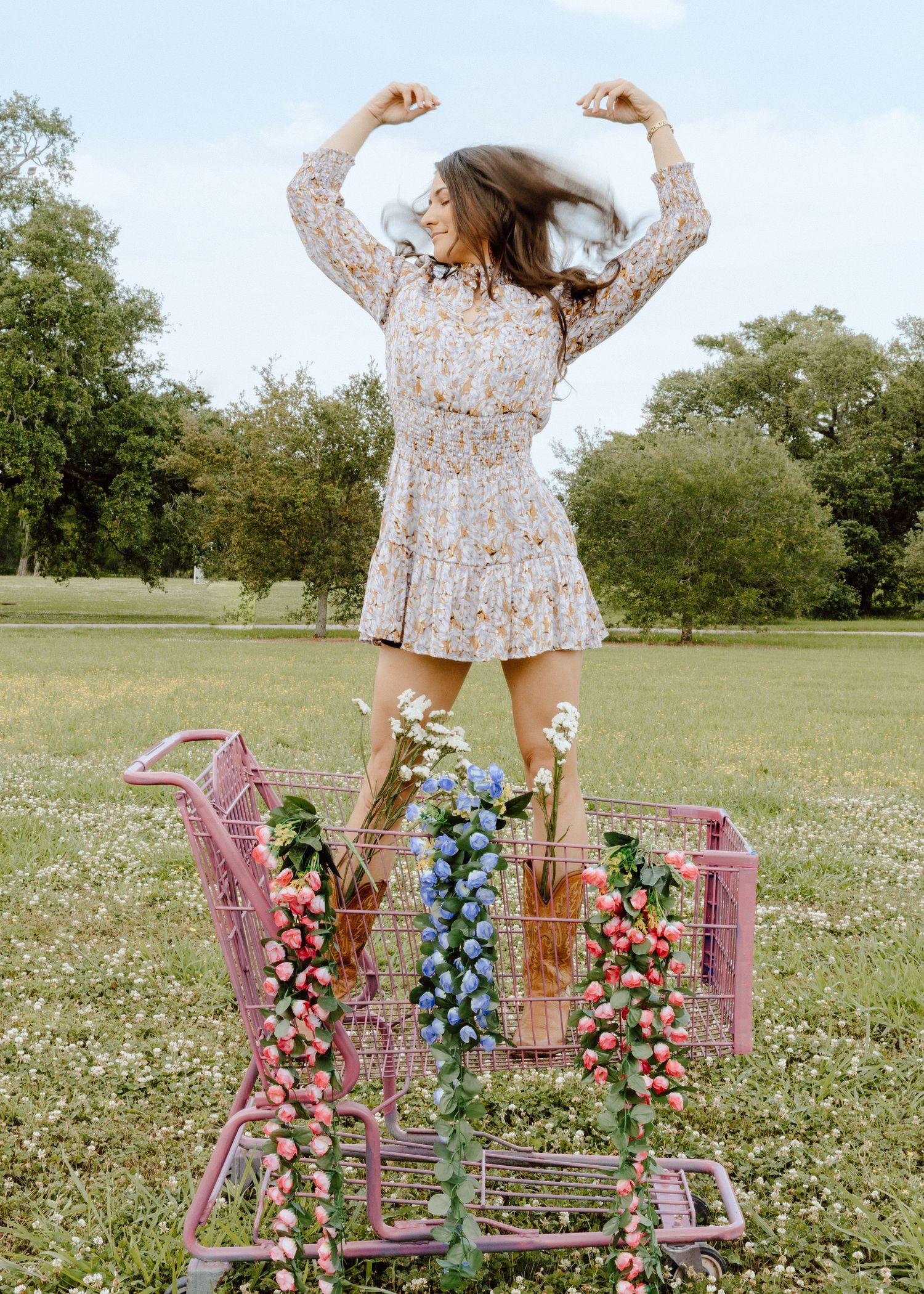 Colorful floral arrangements decorate pink chairs in a sunny meadow filled with white wildflowers.