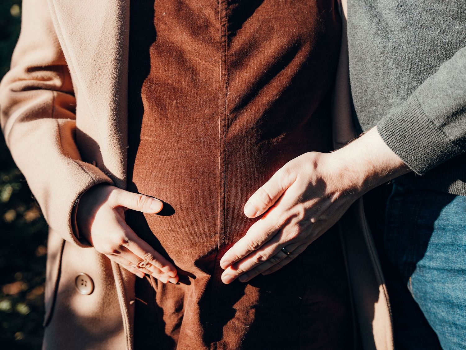 Close-up of hands reaching toward each other against warm-toned clothing.