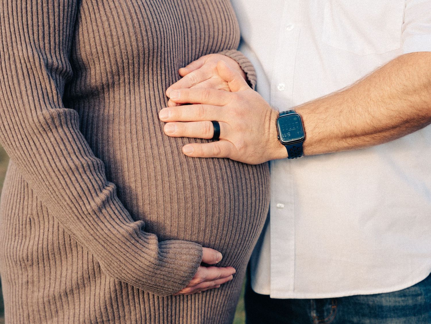 Close-up series showing a person in a brown knit sweater embracing a growing baby bump in natural lighting in Belmont, MA.