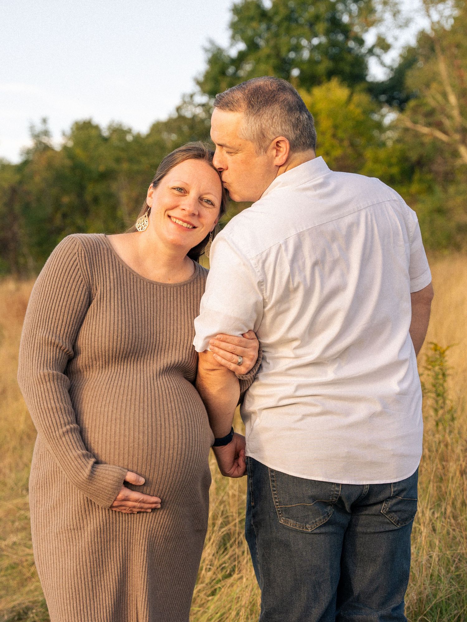 Couple sharing intimate moments outdoors with focus on pregnancy bump in autumn field setting in Belmont, MA.