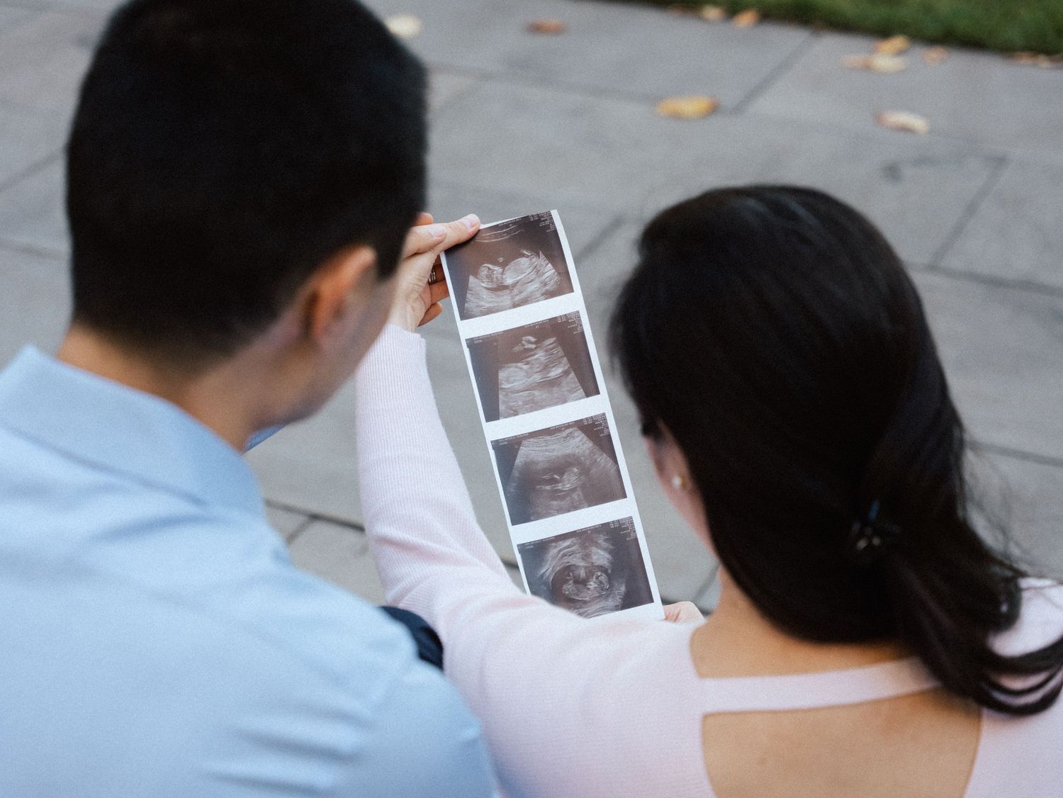A couple examines ultrasound photos together while sitting outside at Harvard campus.
