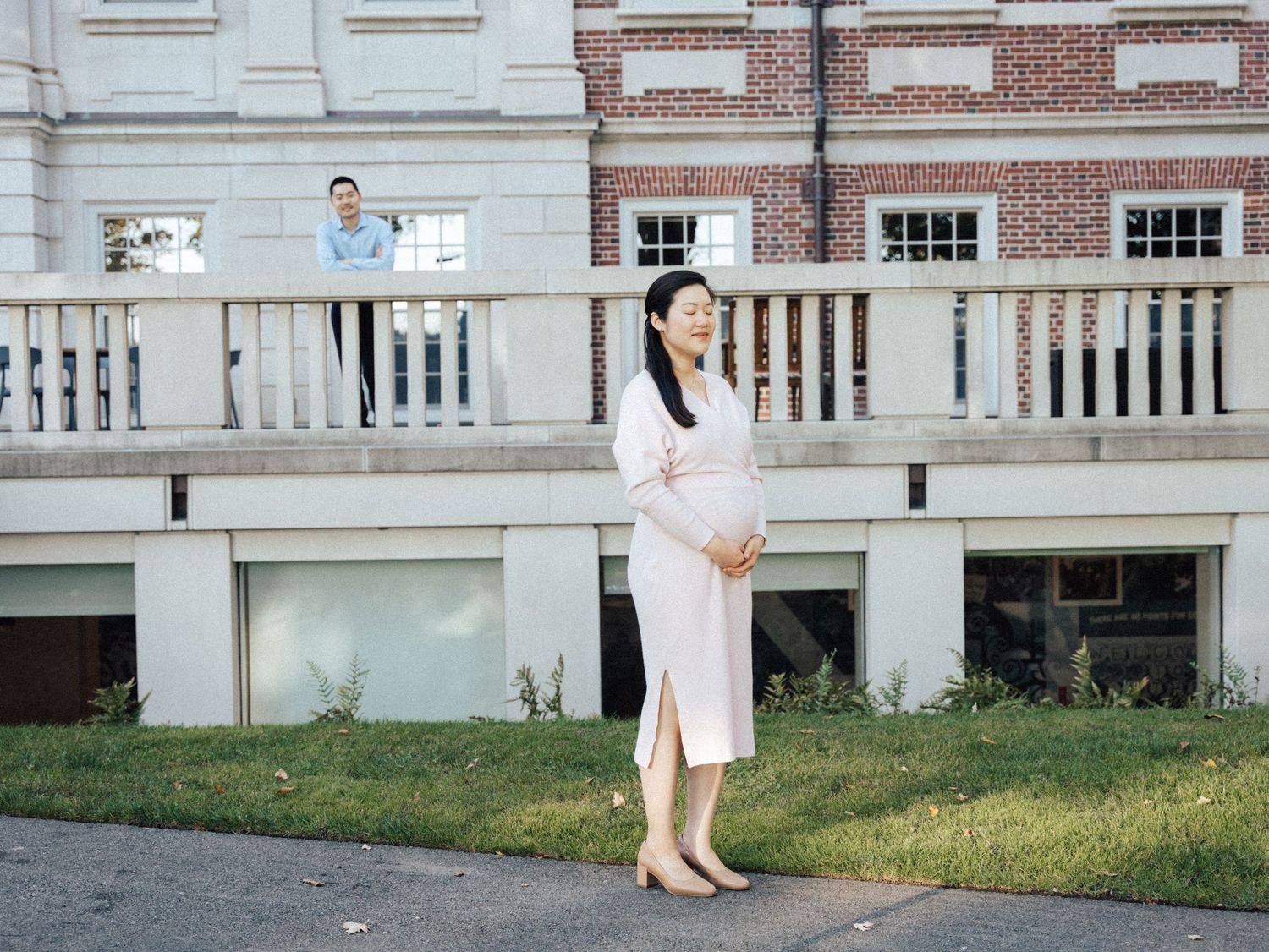 An expectant parent poses in a white dress on a brick building's balcony. at Harvard campus